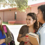 Three female students at California Tribal College chatting with each other outdoors with books in hand